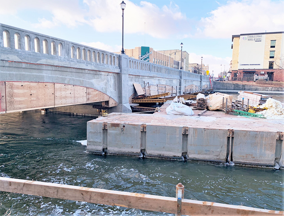 During construction of the West Milwaukee Street Bridge in Janesville, Wisconsin, materials were floated in on barges within the Rock River. 