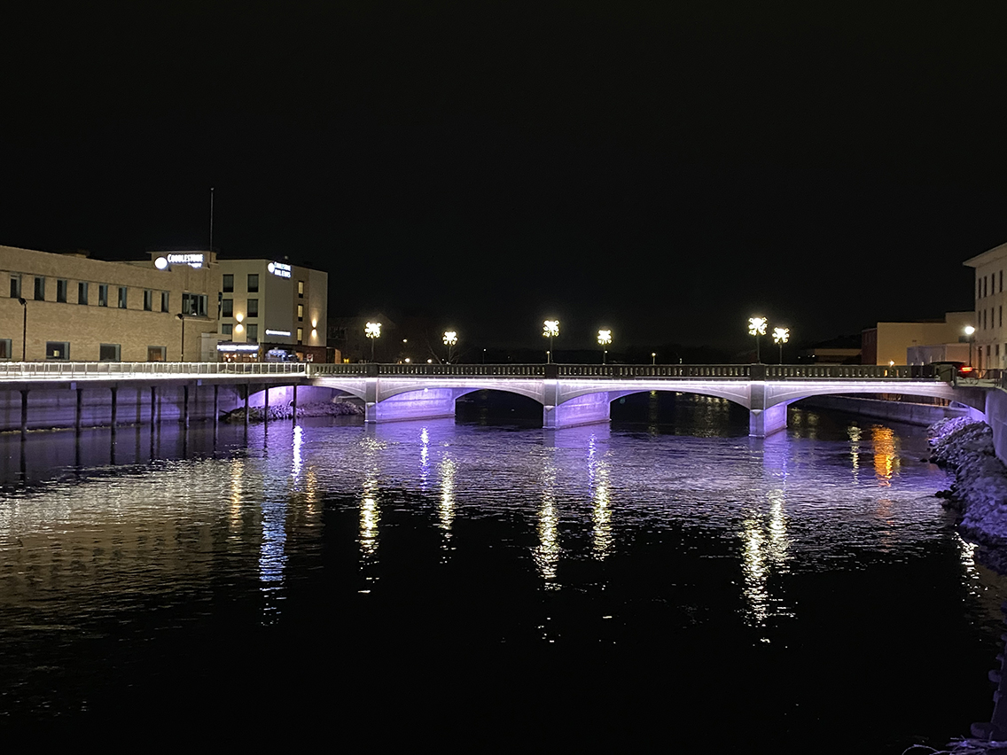 Nighttime shot of the new West Milwaukee Street Bridge in Janesville, Wisconsin, shines purple accent lights onto the waters of the Rock River.