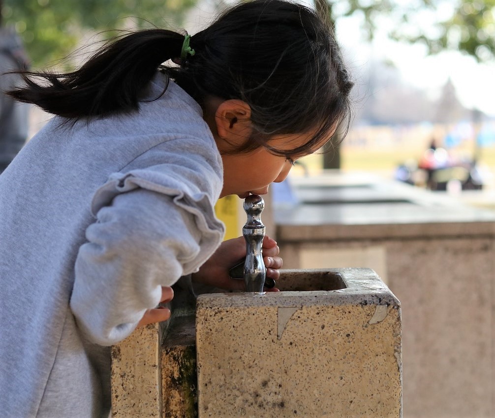 young girl drinks from water fountain