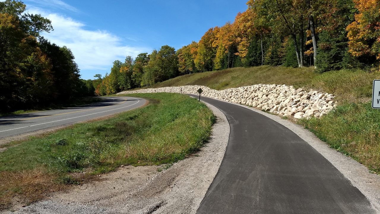 Image of paved bike and pedestrian trail with rock retaining wall and autumn leaves as part of the newly complete Conover-Phelps trail in Phelps, Wisconsin.