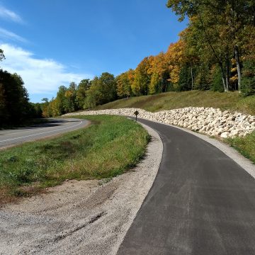 Image of paved bike and pedestrian trail with rock retaining wall and autumn leaves as part of the newly complete Conover-Phelps trail in Phelps, Wisconsin.