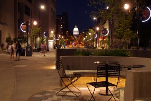 City of Madison State Street Reconstruction - image at night with the Wisconsin Capitol building lit up and cafe seating, nighttime pedestrians.
